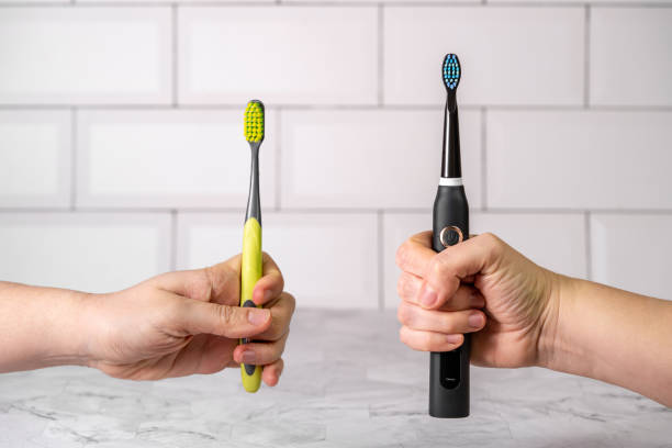 Two hands hold a manual toothbrush and an electric toothbrush.